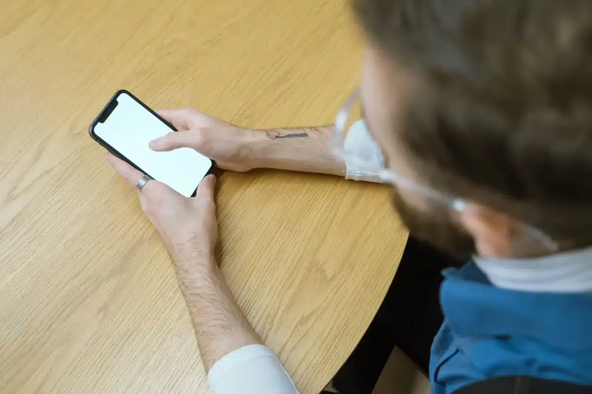 Main d'une personne tenant un smartphone affichant une interface de messagerie professionnelle sur un bureau minimaliste