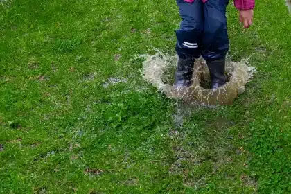 Paire de bottes de pluie anonymes près d'une flaque, parapluie plié à côté