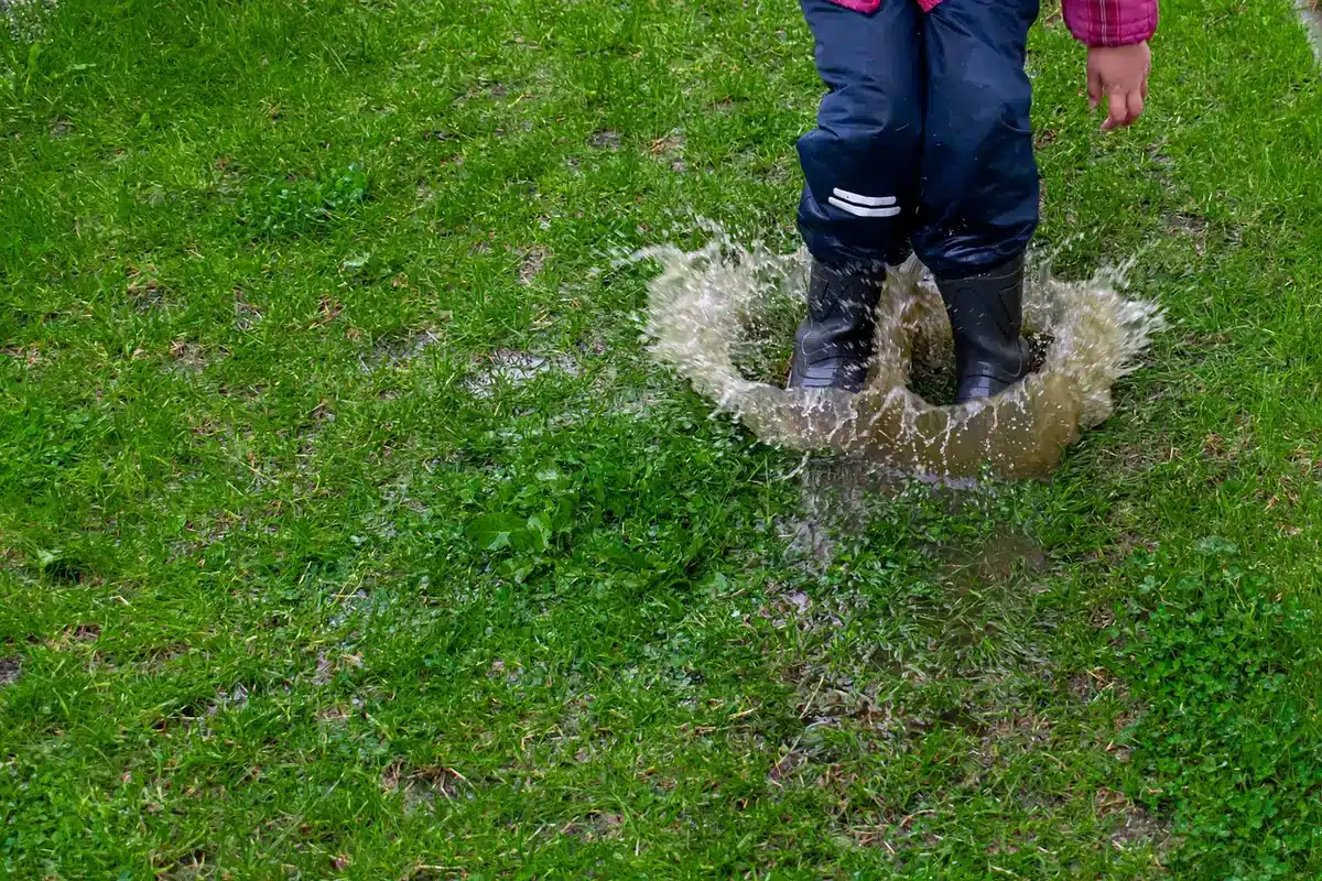 Paire de bottes de pluie anonymes près d'une flaque, parapluie plié à côté