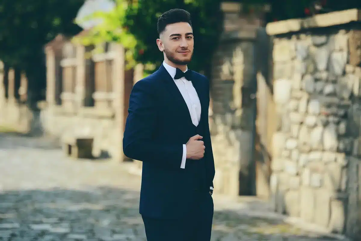 Main ajustant un nœud papillon sur une veste bordeaux dans une cabine de couture