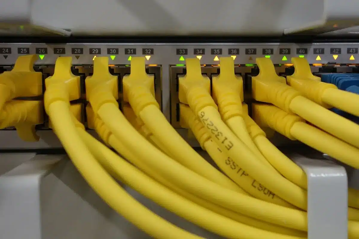 Salle de serveurs anonyme avec racks et câbles, main gantée devant un écran flou